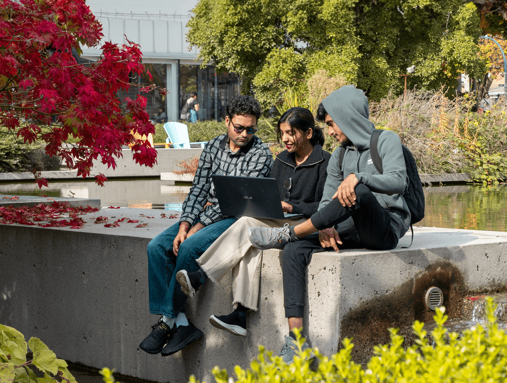 Students sitting in a campus garden working on a laptop