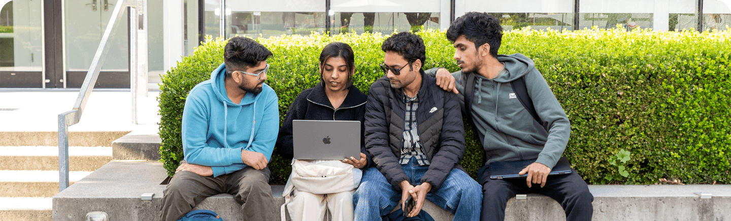 Students sitting in a campus garden working on a laptop